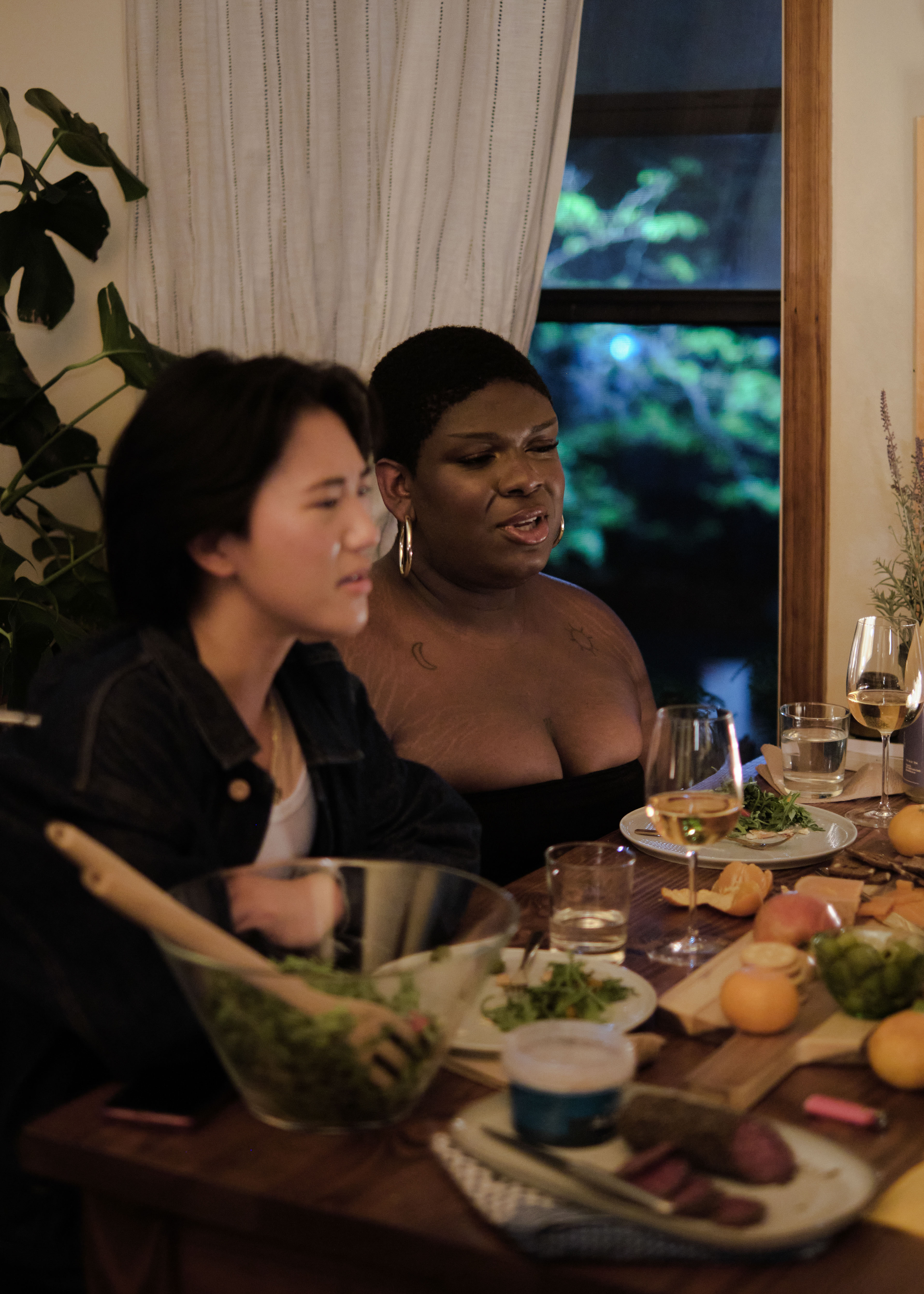 A non-binary trans woman and a non-binary trans man at a dinner party with friends